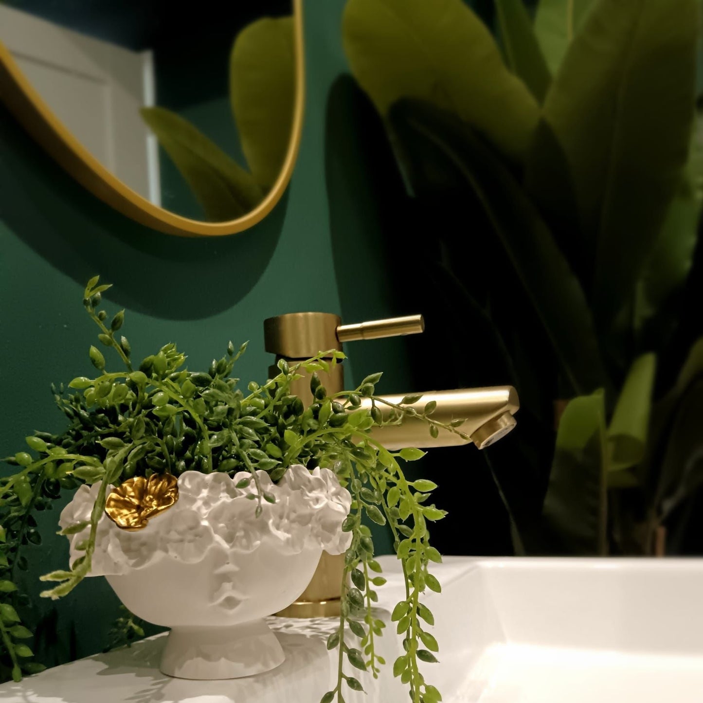 Coupelle Fleurie en céramique blanche avec des détails floraux et feuille dorée, mise en scène dans une salle de bain élégante avec robinet doré.